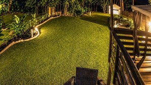 Une pelouse bien entretenue, agrémentée d’une terrasse en bois avec garde-corps, le tout entouré d’une végétation luxuriante.