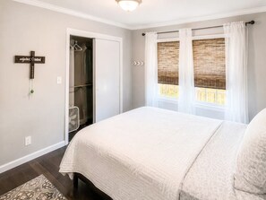 A bedroom with a bed, a closet, a window with curtains, and a wall-mounted cross. - Tucked away in Tucker (Tucker)