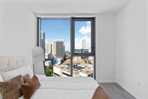 Quarto com uma janela ampla, uma cama e vista para a cidade.