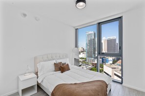 A modern bedroom with a large window, a bed, a nightstand, and a view of the cityscape. - 2-bedroom condo in marvelous Miami Views in the perfect spot! (Miami)