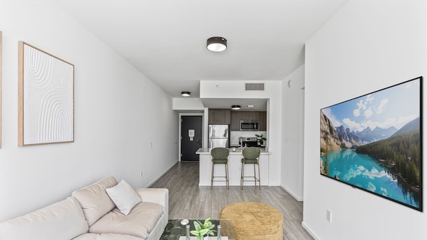 A modern living room with a sofa, a coffee table, and a painting of a mountain lake. - 2-bedroom condo in marvelous Miami Views in the perfect spot! (Miami)