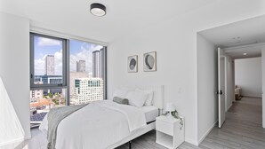 A modern bedroom with a large window, a bed, a bedside table, and a view of the cityscape. - 2-bedroom condo in marvelous Miami Views in the perfect spot! (Miami)