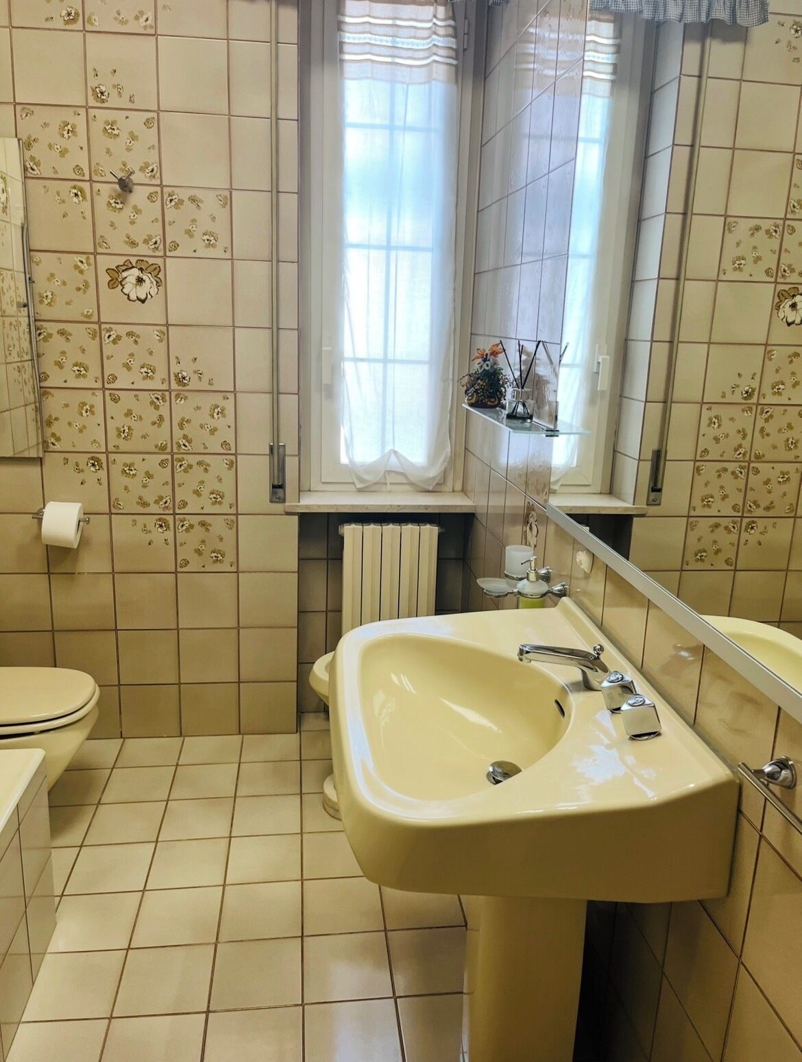Et badeværelse med toilet, håndvask og et vindue med gardiner.