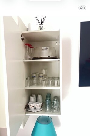 Ein weißes Schränkchen mit Regalen, auf denen Gläser, ein Diffusor und eine türkisfarbene Vase stehen.