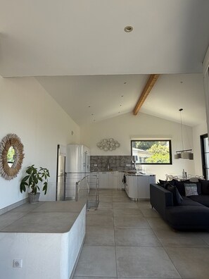 A modern kitchen with a central island, a dining area with a sofa, and a view of the outdoors through a window. - Vacation Home for Rent (Belgodère)