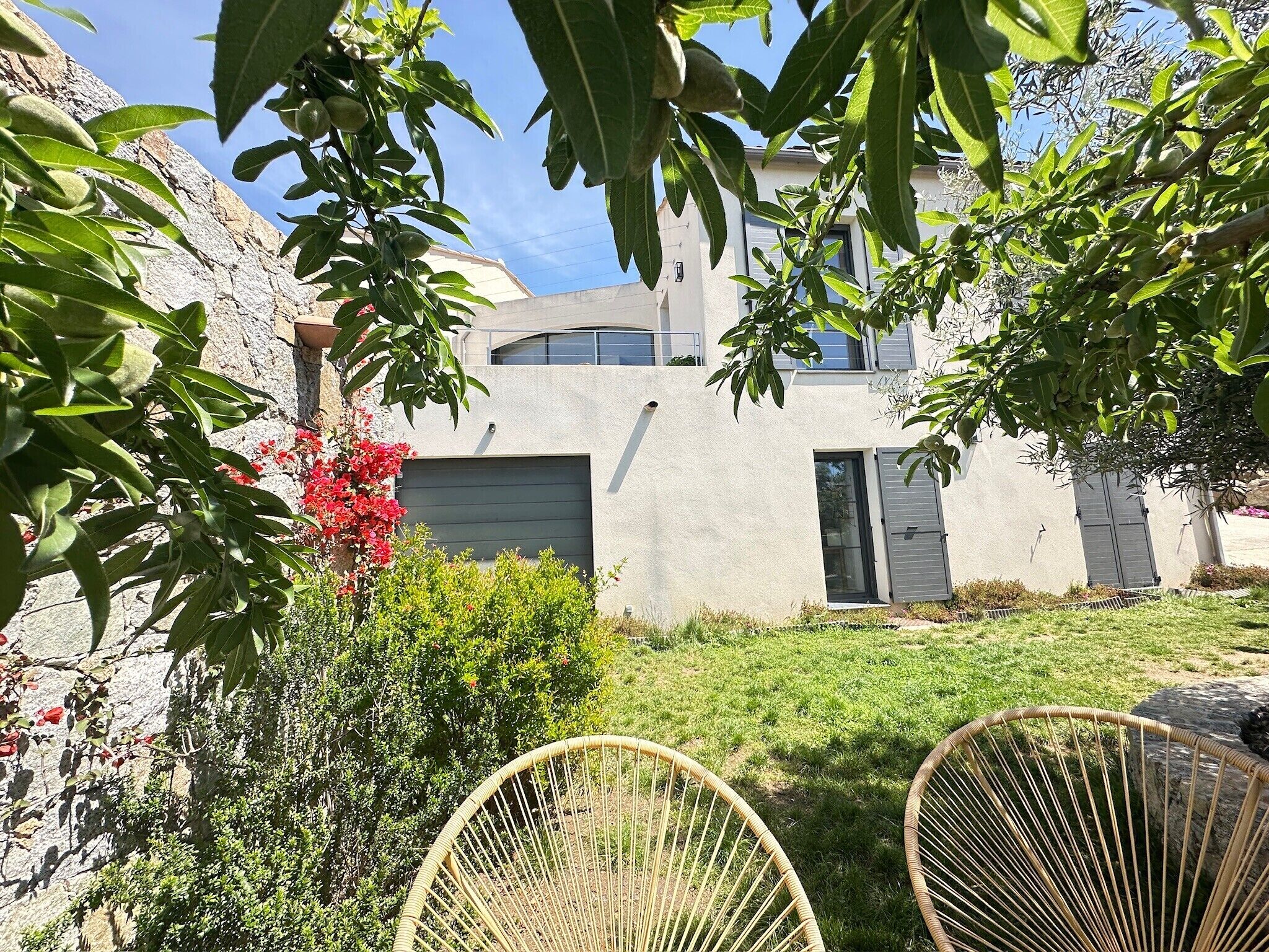 Ein modernes Haus mit einer Steinaußenwand, einem Rasen und zwei Korbstühlen.