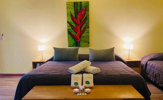 Una habitación de hotel con una cama grande, dos mesitas de noche, un banco de madera y una obra de arte en la pared.