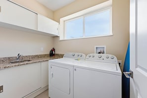 A laundry room with a washer and dryer, a countertop with a sink, and a window above the dryer. - Stylish 4 Ensuite Home Near Disney, free BBQ grill (Four Corners)