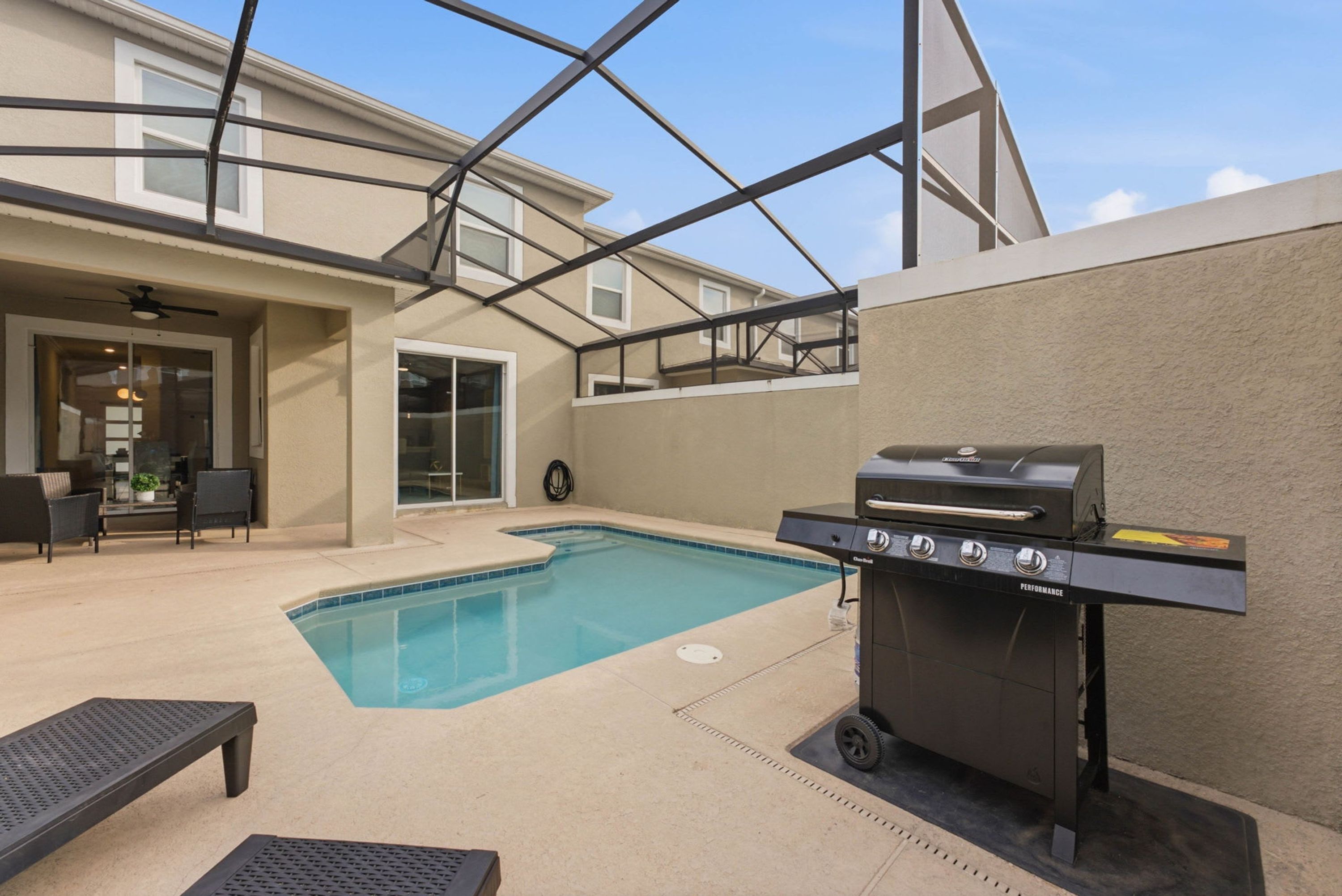 An outdoor pool area with a barbecue grill, lounge chairs, and a covered patio.