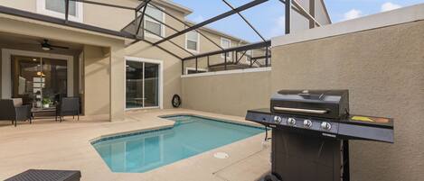An outdoor pool area with a barbecue grill, lounge chairs, and a covered patio.