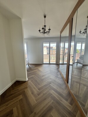 Una habitación espaciosa con suelo de madera en espiga, grandes puertas correderas de vidrio que dan a un balcón y una araña.