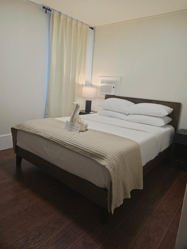 A hotel room with a bed, a nightstand, a lamp, and a window with curtains.