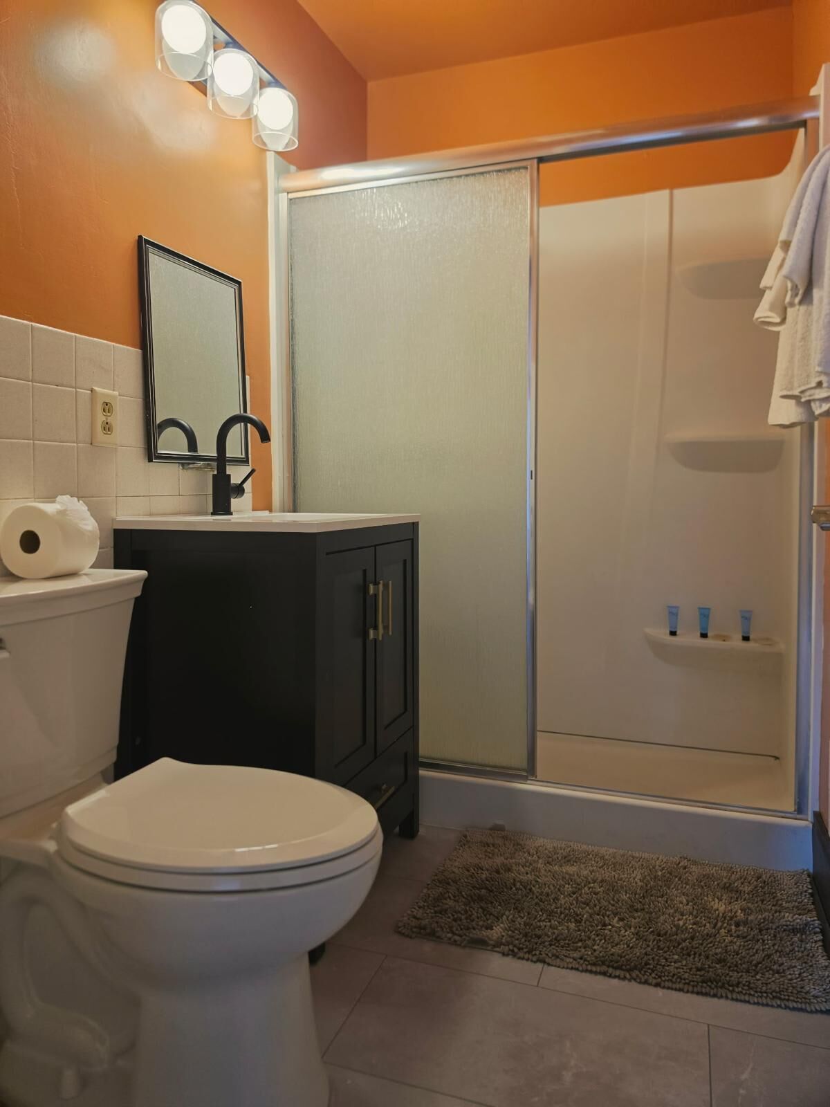A bathroom with a toilet, sink, mirror, and shower.