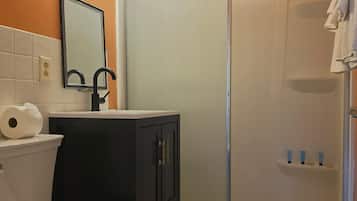 A bathroom with a toilet, sink, mirror, and shower.