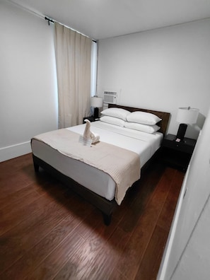 A hotel room with a bed, a nightstand, a lamp, and a window with curtains.