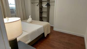 Une chambre à coucher comprenant un lit, une table de chevet avec une lampe, une armoire avec une penderie et une vue par la fenêtre.