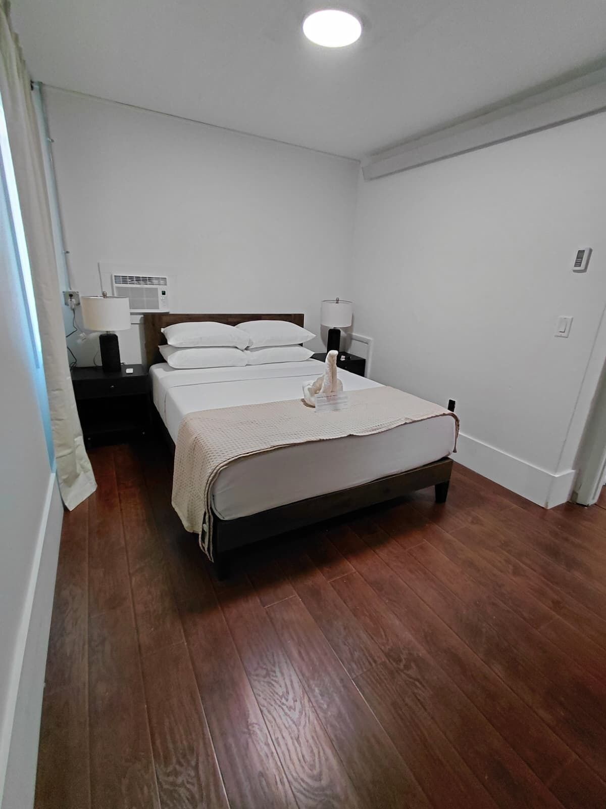 A bedroom with a bed, bedside lamps, a nightstand, and a wall-mounted air conditioning unit.