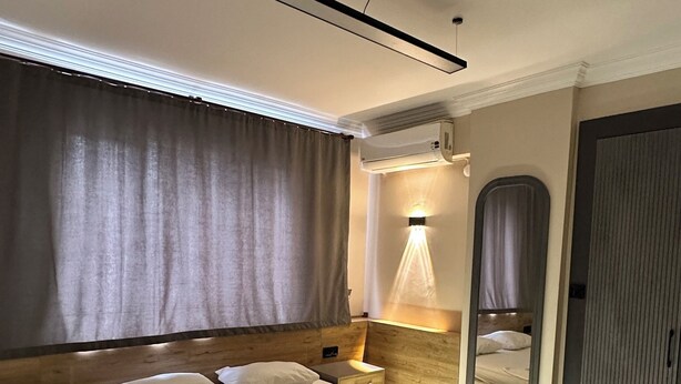 Een moderne slaapkamer met een groot bed, nachtkastjes, een spiegel en een plafondlamp.