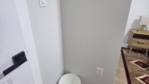 Un coin de pièce avec une porte blanche, un seau blanc et un interrupteur sur le mur.