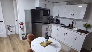 Une cuisine moderne avec des meubles blancs, un réfrigérateur en acier inoxydable et un coin repas comprenant une table ronde et deux chaises.