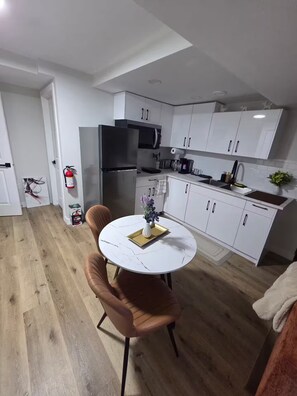 Une cuisine moderne avec des meubles blancs, un réfrigérateur en acier inoxydable et un coin repas comprenant une table ronde et deux chaises.