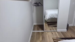 Une chambre avec un plancher en bois, un lit, une armoire et un miroir.