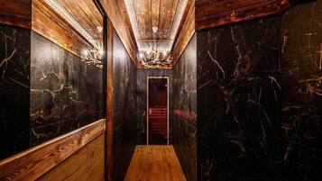 A narrow hallway with wooden walls and a marble floor, leading to a door with a red frame.