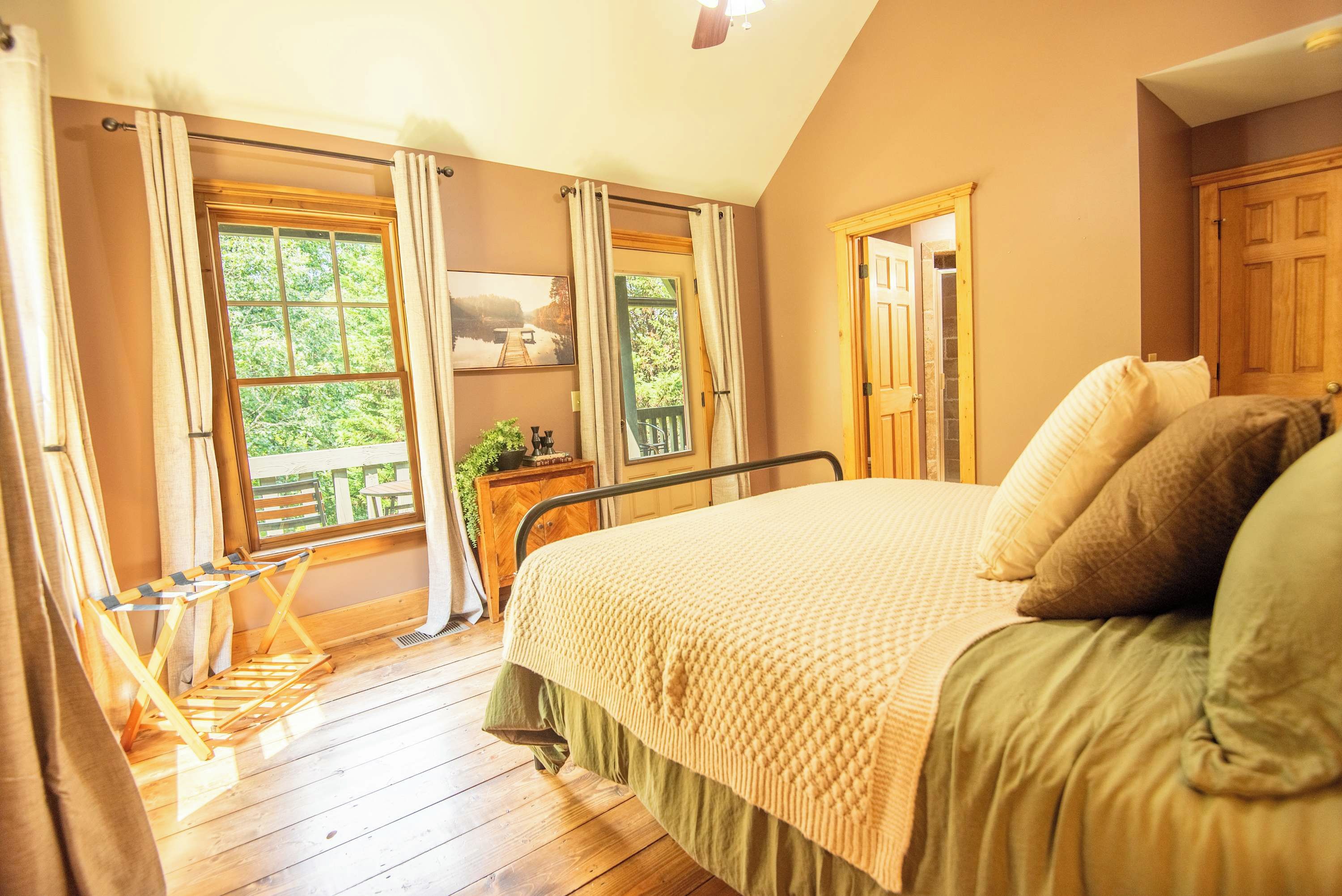 A bedroom with a large bed, wooden flooring, and a view of a dock through the windows.