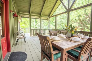 Eine überdachte Veranda mit einem Holztisch, gedeckt für ein Essen, umgeben von Stühlen.
