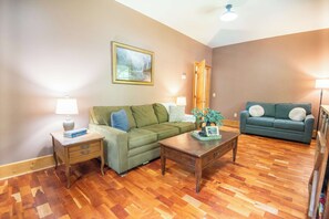 A living room with a green sofa, a blue sofa, wooden flooring, and a painting on the wall.