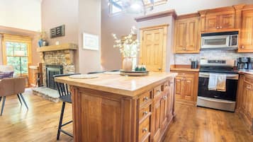 A kitchen with wooden cabinets, a central island, a stone fireplace, and a dining area with a chair and table.