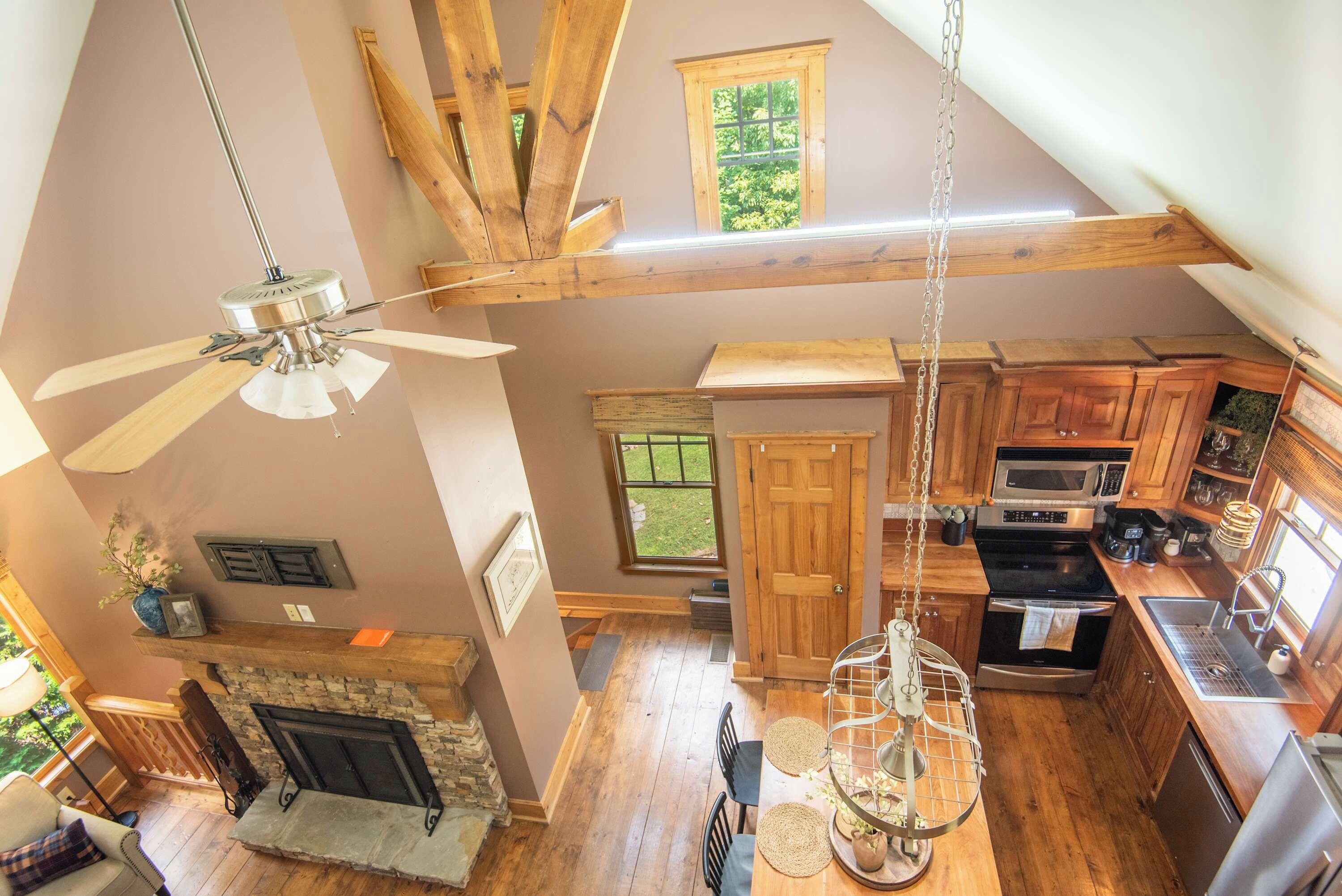 A spacious loft-style room with a high ceiling, exposed wooden beams, a fireplace, a dining area with a table and chairs, and a kitchen with modern appliances.