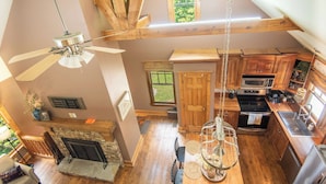 A spacious loft-style room with a high ceiling, exposed wooden beams, a fireplace, a dining area with a table and chairs, and a kitchen with modern appliances. - *NEW!* Cozy Watts Bar Getaway for Families & Friends (Rhea County)