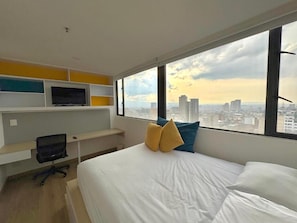 A hotel room with a bed, a TV on a shelf, and a city view. - Hotel Happa Hub (Bogota)