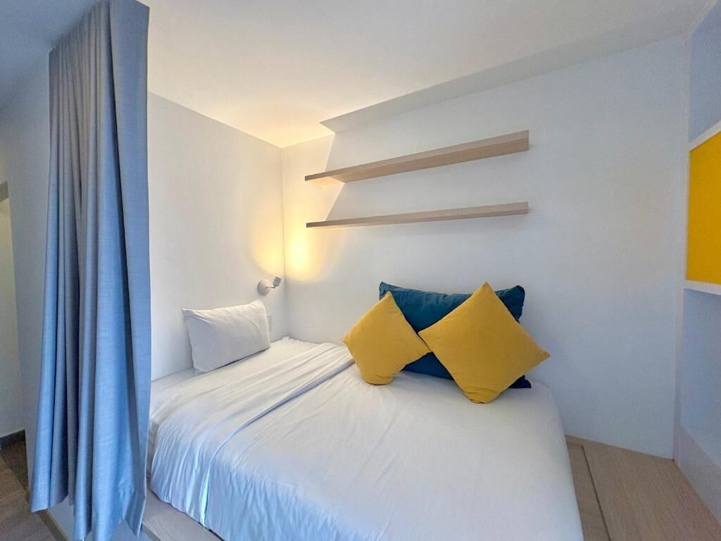 A hotel room with a bed, curtains, a wall-mounted shelf, and a bedside lamp.