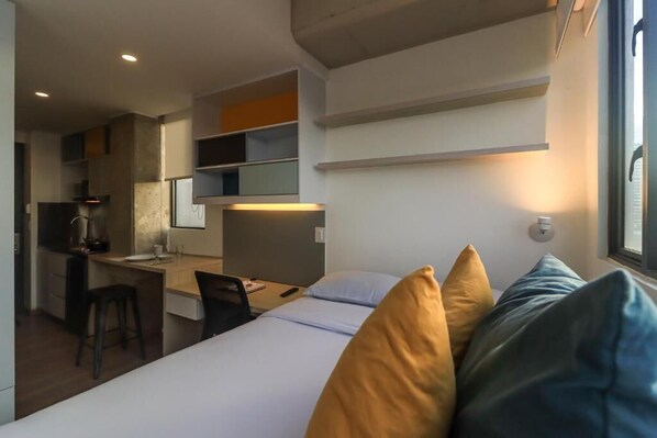 Una habitación de hotel compacta con cama, escritorio y zona de kitchenette.