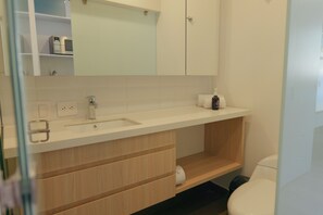 Un baño moderno con lavamanos blanco, espejo y tocador de madera.