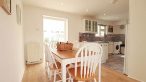 A modern kitchen with white cabinetry, a dining table with chairs, and a built-in washing machine. - Cloudbreak (Wadebridge)