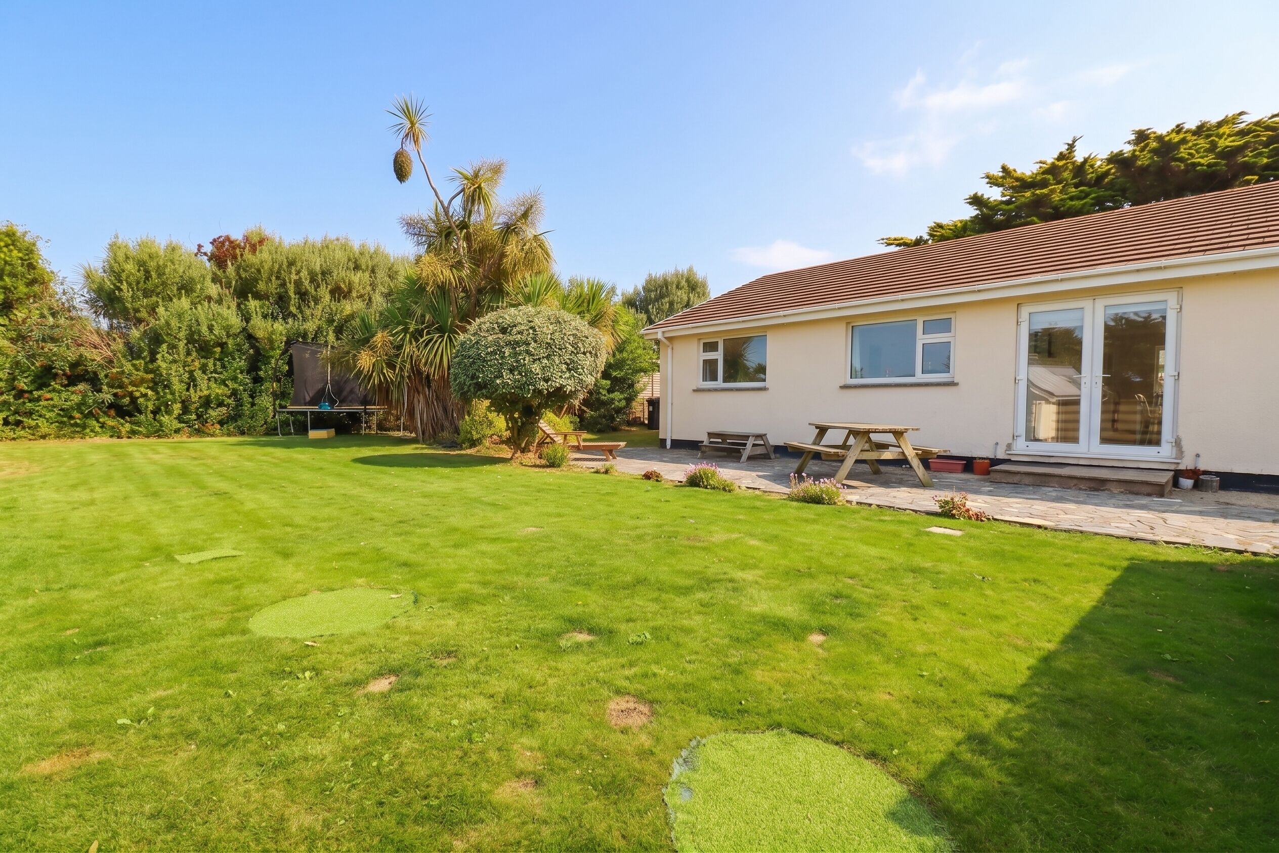 A house with a well-maintained lawn, a patio with a table and chairs, and a variety of trees and shrubs in the garden.