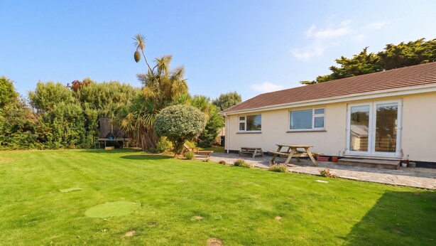 A house with a well-maintained lawn, a patio with a table and chairs, and a variety of trees and shrubs in the garden. - Cloudbreak (Wadebridge)