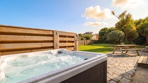 A hot tub in an outdoor setting with a wooden deck and a stone patio. - Cloudbreak (Wadebridge)
