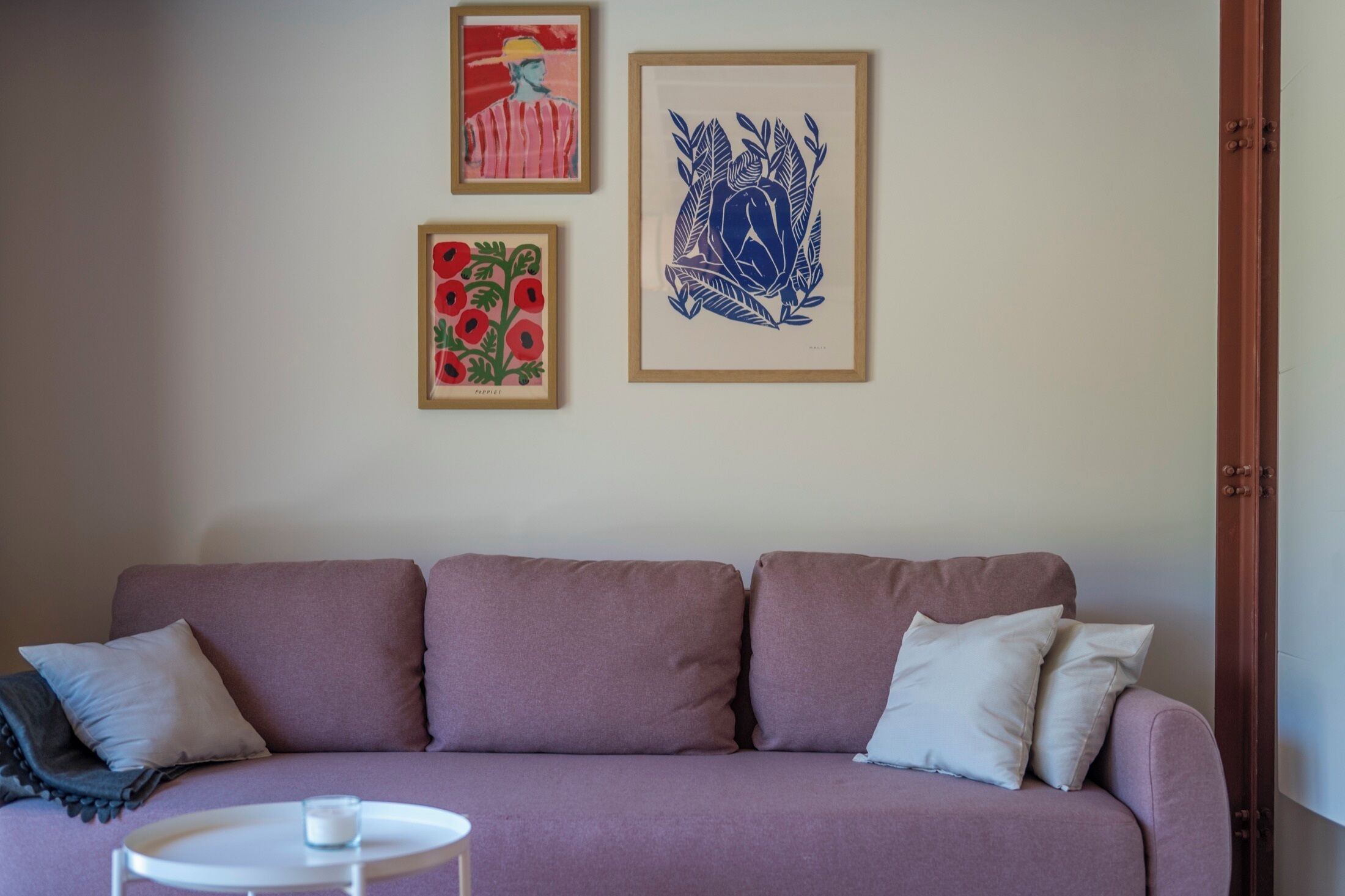 Un salon comprenant un canapé, deux coussins, une petite table ronde et trois œuvres d’art encadrées accrochées au mur.
