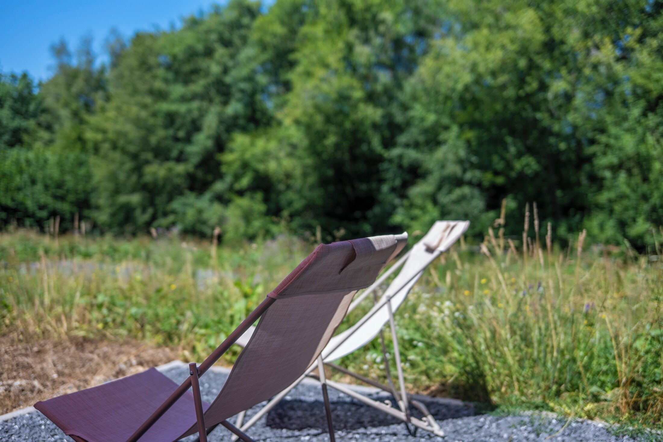 Deux chaises pliantes sont posées sur un sol de gravier, avec un paysage naturel en arrière-plan.
