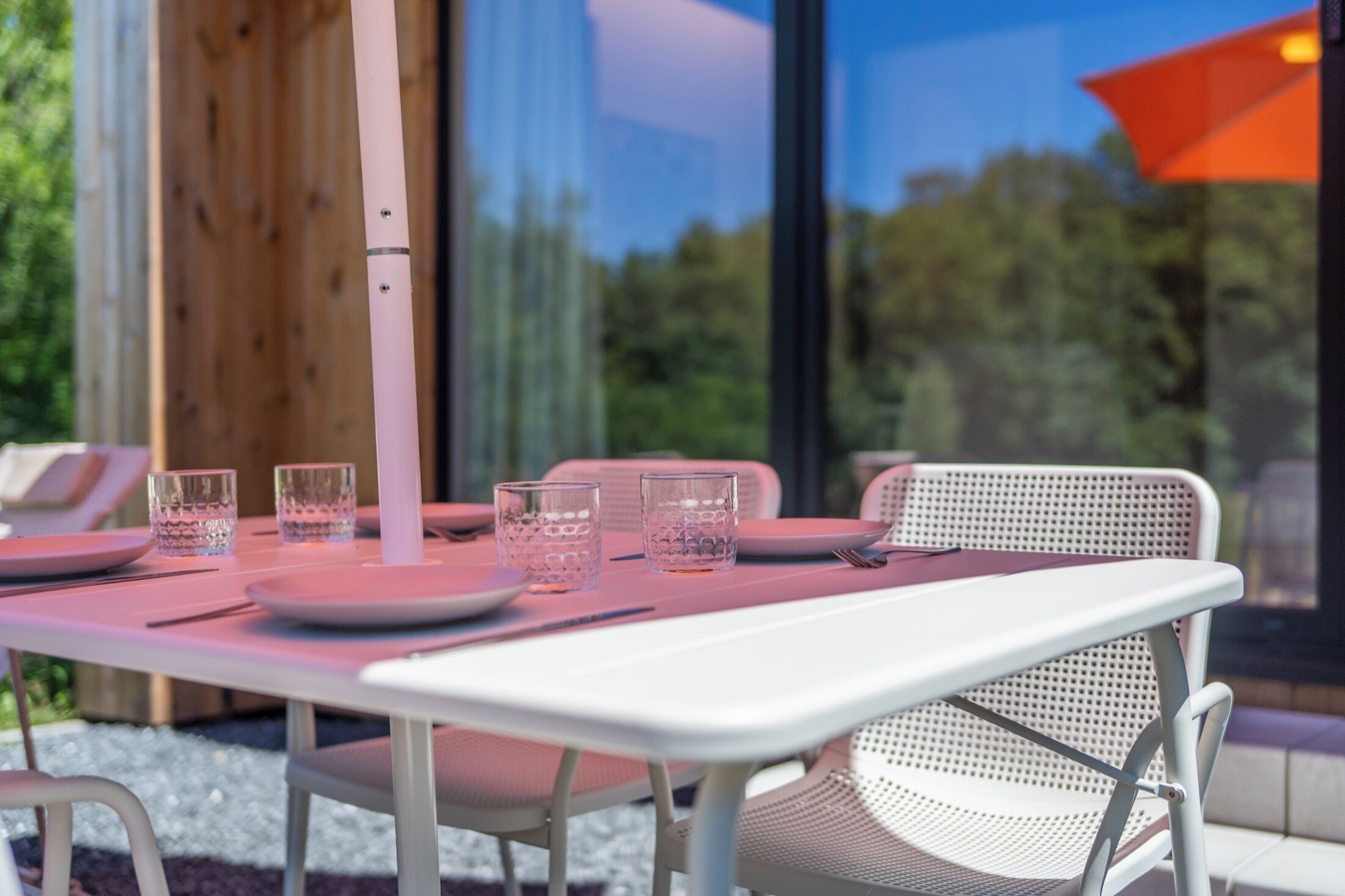 Une table à manger dressée avec des sets de table roses, des verres transparents et des assiettes blanches, agrémentée de chaises au design moderne.