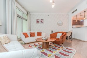 A modern living room with a white sofa, an orange armchair, a round coffee table, and a colorful rug. - HAVN - 2 Bed in Dubai Marina, 5 mins to Tram (Dubai)