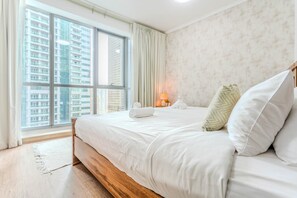 A hotel room with a large window, a bed with white linens, and a nightstand with a lamp. - HAVN - 2 Bed in Dubai Marina, 5 mins to Tram (Dubai)