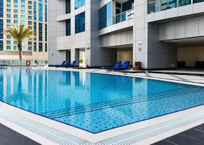 Ein Pool mit blauen Fliesen, umgeben von einem modernen Gebäude mit großen Fenstern und einer Palme.