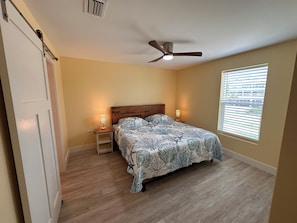 A bedroom with a bed, two bedside lamps, a ceiling fan, and a window with blinds.