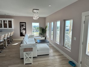 A spacious living area with a large sectional sofa, a dining table with bar stools, and a view of the outdoors through multiple windows.
