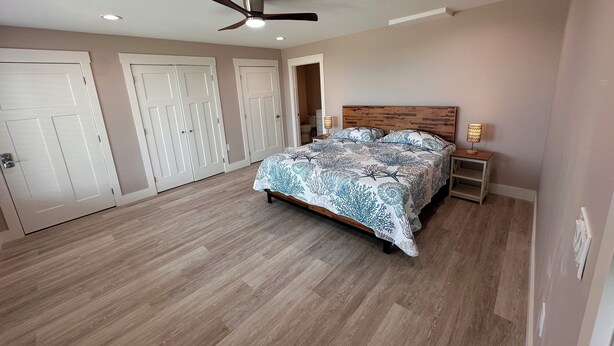 A bedroom with a bed, a ceiling fan, and a nightstand with a lamp.